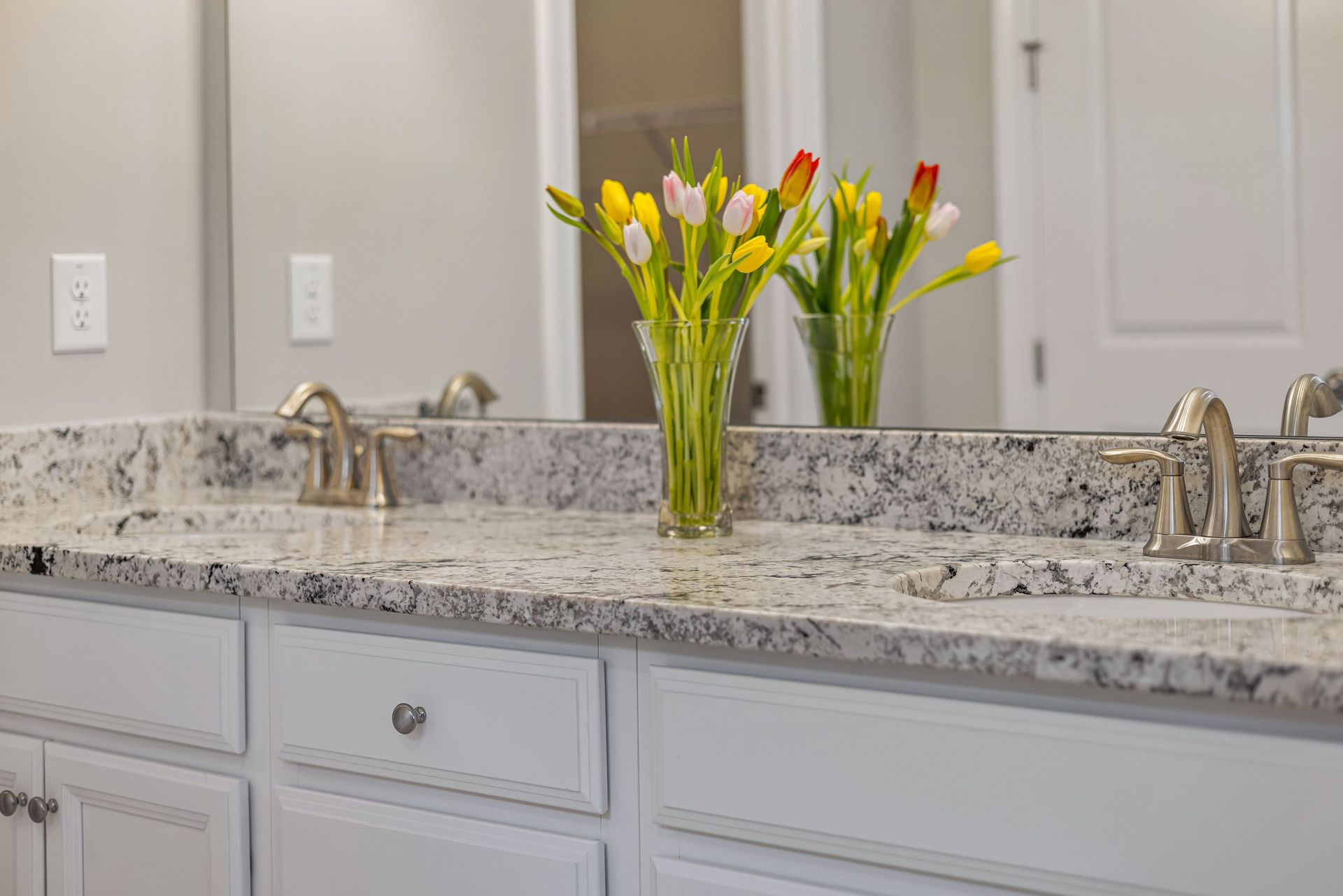 Modern bathroom with white granite countertop and a vase of colorful tulips.